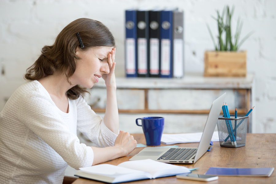 Young stressed businesswoman sitting in front of laptop and touching head with pained expression. Business person feeling pain suffering from migraine after working on pc overworked or depressed